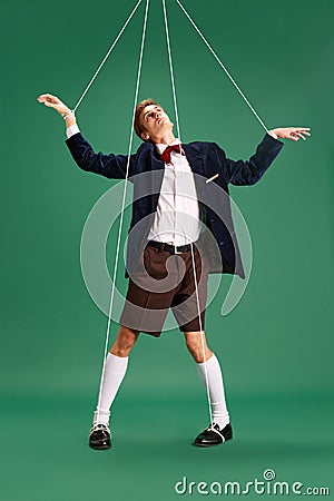 Social manipulation and pressure. Young guy, marionette on string against green studio background Stock Photo