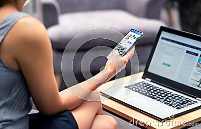 Social media profile page in smartphone screen at work. Woman looking at feed, status update or post with mobile phone. Stock Photo