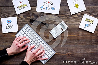 Social media promotion. Work desk with socail media icons. Dark wooden background top view. Hand is typing Stock Photo