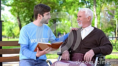 Social worker reading book for disabled pensioner, leisure in park, volunteering Stock Photo