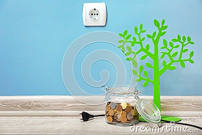 Socket, decorative tree and jar with coins on floor. Electricity saving concept Stock Photo