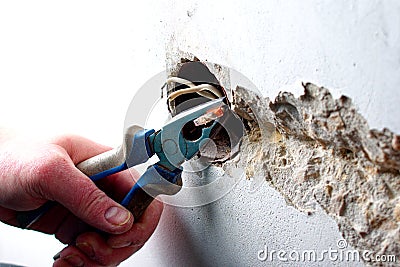 A socket outlet with exposed aluminum wires. A handyman with psoriasis is pinching the wires with pliers. Wiring repair concept Stock Photo