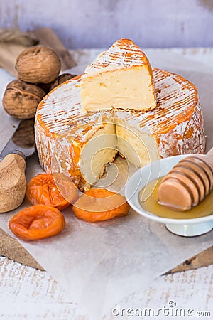 Soft cheese with cut off slice creamy texture, orange rind with mold, French, German, Alps, honey dipper, walnuts, dried apricots, Stock Photo