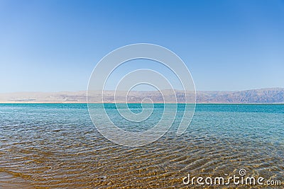 Soft crystal clear water in the sea at sunny day with mountains against the background. Dead sea coastline. Stock Photo