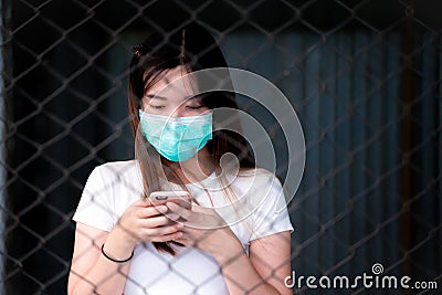 Soft focus, Asian women stands using smartphone behind iron fence. Black wall background. Stock Photo
