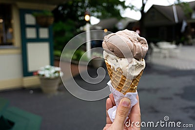 Soft focus of Ice Cream Cone. A hand holding an ice cream cone with scoop of chocolate and vanilla flavor. Blurry ice cream shop Stock Photo