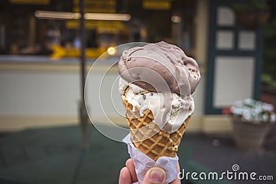 Soft focus of Ice Cream Cone. A hand holding an ice cream cone with scoop of chocolate and vanilla flavor. Blurry ice cream shop Stock Photo