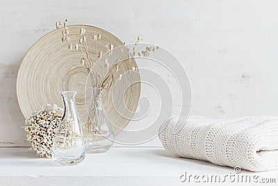 Soft home decor of glass vase with spikelets and knitted fabric on white wood background. Stock Photo