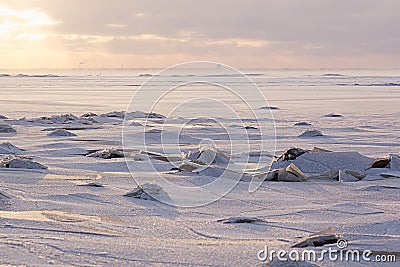 Soft light golden sunset in winter over frozen coast with broken ice, horizon, sunbeams and shiny snow, landscape in pastel pink. Stock Photo