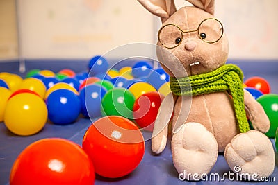 Soft toy rabbit with glasses and scarf for kids with colored balls. Bright children& x27;s toys. Stock Photo