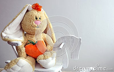 Soft toy-yellow hare with a heart in his hands on a wooden horse on a gray background space for text Stock Photo