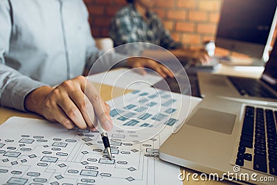 Software developer is pointing to the paper working and analyzing together the code written into the program on the computer Stock Photo