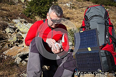 The solar panel attached to the tent. The man sitting next to mobile phone charges from the sun. Stock Photo