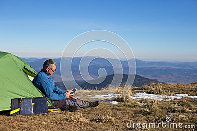 The solar panel attached to the tent. The man sitting next to mobile phone charges from the sun. Stock Photo