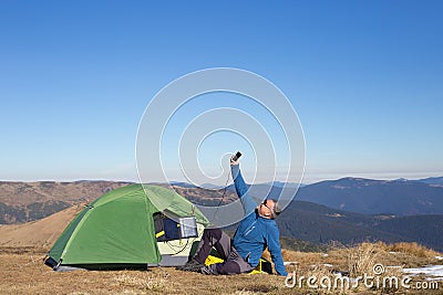 The solar panel attached to the tent. The man sitting next to mobile phone charges from the sun. Stock Photo