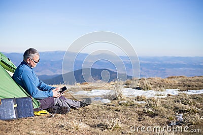 The solar panel attached to the tent. The man sitting next to mobile phone charges from the sun. Stock Photo