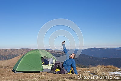 The solar panel attached to the tent. The man sitting next to mobile phone charges from the sun. Stock Photo