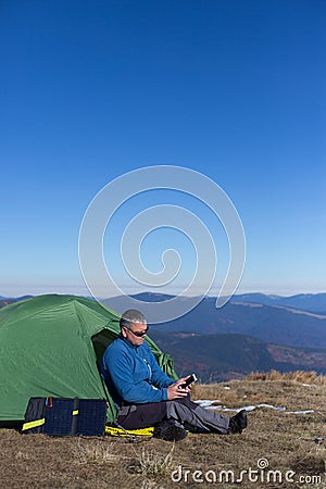 The solar panel attached to the tent. The man sitting next to mobile phone charges from the sun. Stock Photo