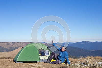 The solar panel attached to the tent. The man sitting next to mobile phone charges from the sun. Stock Photo