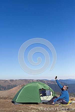 The solar panel attached to the tent. The man sitting next to mobile phone charges from the sun. Stock Photo