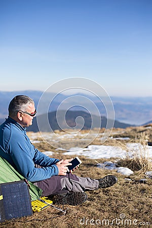 The solar panel attached to the tent. The man sitting next to mobile phone charges from the sun. Stock Photo