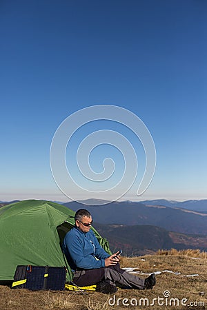 The solar panel attached to the tent. The man sitting next to mobile phone charges from the sun. Stock Photo