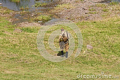 A soldier in Soviet uniform, on the river bank, with an assault rifle, from the back Editorial Stock Photo