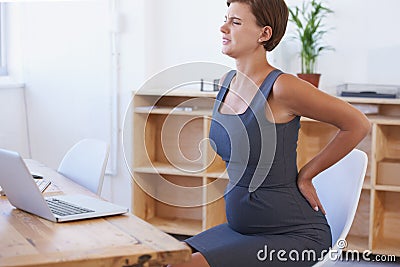 Soldiering through the pain. A pregnant businesswoman struggling with backache at her office desk. Stock Photo