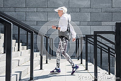 Solemn senior woman jogging outdoor on stone steps with handrails Stock Photo