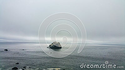 Solitary boulder against moody ocean sky. Stark foggy vanishing point. Background. Minimalism. Stock Photo