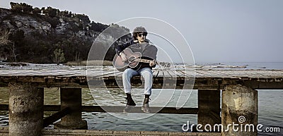 Solitary Boy Playing Guitar on the Pier Stock Photo