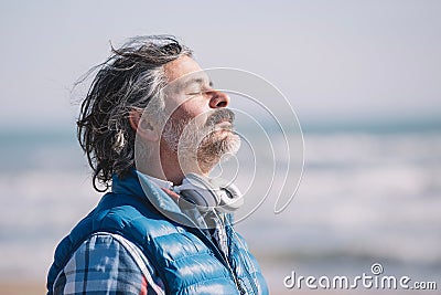 Solitary male figure stands on a sandy beach wearing headphones with his eyes closed Stock Photo