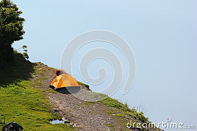 Solitary orange tent camped near water edge Stock Photo