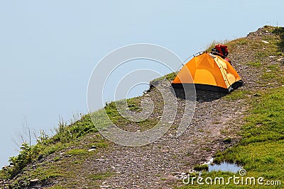 Solitary orange tent camped near water edge Stock Photo