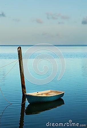 Solitary small boat moored at soft cyan blue sunrise. Stock Photo