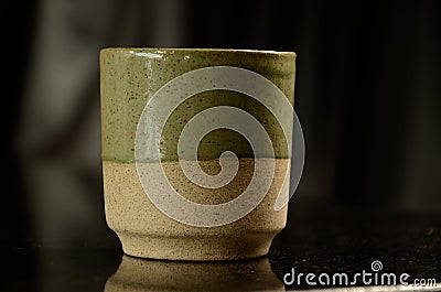 A solitary small ceramic glass, in green and beige on top of a black stone countertop, where you can drink water, cachaÃ§a or Stock Photo