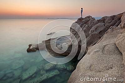 Solitude girl watching sunrise high up on cliff by sea Stock Photo