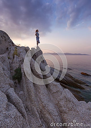 Solitude girl watching sunset high up on cliff by sea Stock Photo