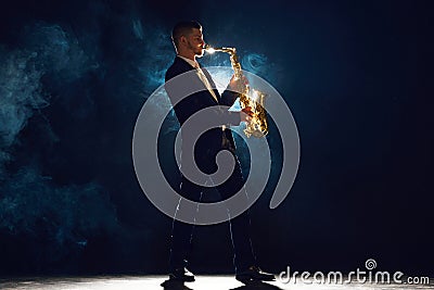 Solo saxophonist in concert outfit performing with intense expression on stage with backlight against dark background Stock Photo