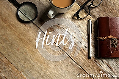 Top view of magnifying glass, coffee, glasses, pen and notebook on wooden background written with Hints Stock Photo