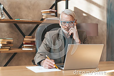 Solution to the problem. A provincial businessman is concentrating on writing an idea on paper. Sits at the desktop in the office Stock Photo