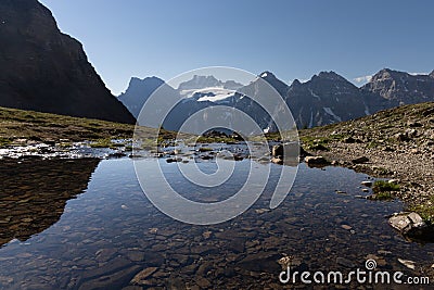 Snow covered peaks in the Canadian Rockies on a summer day with reflections in a small lake Stock Photo