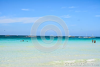 Some tourists swim and take pictures in the White Beach of Boracay with the boats behind them ready for the excursions Editorial Stock Photo