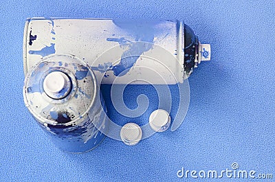 Some used blue aerosol spray cans and nozzles with paint drips lies on a blanket of soft and furry light blue fleece fabric. Class Stock Photo