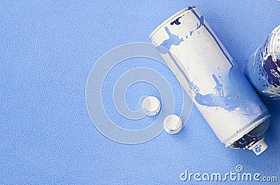 Some used blue aerosol spray cans and nozzles with paint drips lies on a blanket of soft and furry light blue fleece fabric. Class Stock Photo