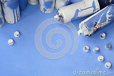 Some used blue aerosol spray cans and nozzles with paint drips lies on a blanket of soft and furry light blue fleece fabric. Class Stock Photo