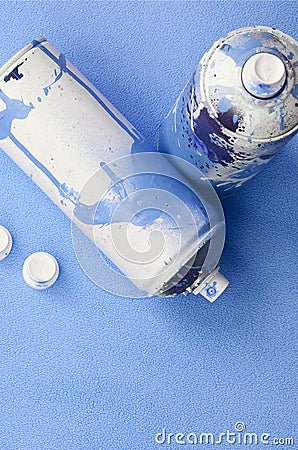 Some used blue aerosol spray cans and nozzles with paint drips lies on a blanket of soft and furry light blue fleece fabric. Class Stock Photo