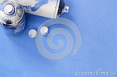 Some used blue aerosol spray cans and nozzles with paint drips lies on a blanket of soft and furry light blue fleece fabric. Class Stock Photo