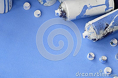 Some used blue aerosol spray cans and nozzles with paint drips lies on a blanket of soft and furry light blue fleece fabric. Class Stock Photo