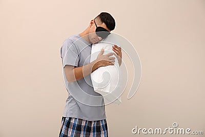 Somnambulist in eye mask with soft pillow on beige background, space for text. Sleepwalking Stock Photo
